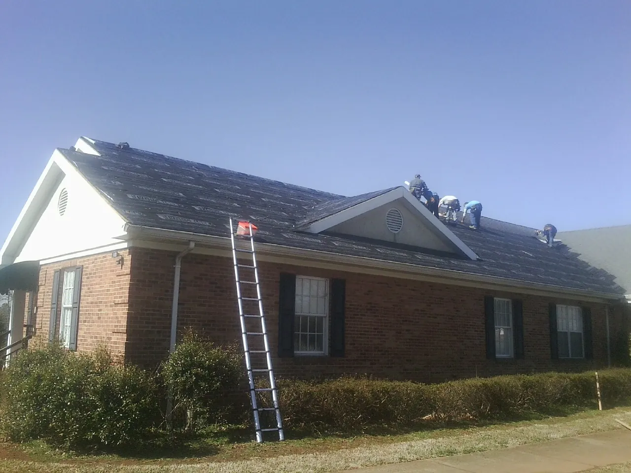 Crew tearing shingles off a brick ranch roof with a ladder set — Emergency Roof Repair work by our crew in Fort Oglethorpe