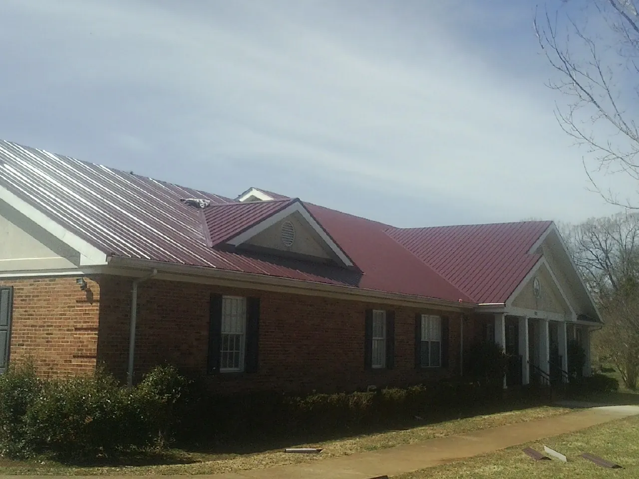 Red metal roof with gabled entries on a long brick building, from a Hail Damage Roof Repair job in Fort Oglethorpe