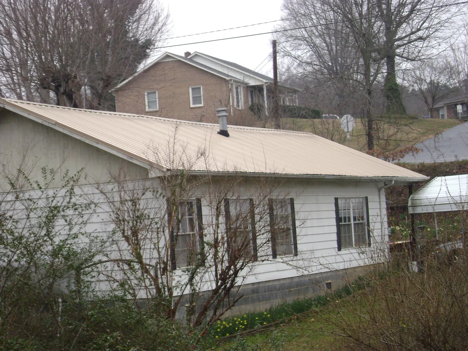 Tan metal roof on a white sided house set into a hillside — Commercial Roofing by Roofing Brothers in Fort Oglethorpe